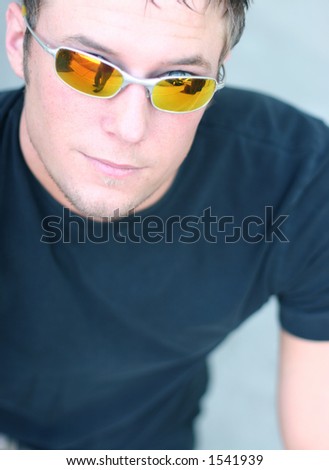 Young man is wearing orange tinted metal sunglasses and black shirt and is looking straight towards you