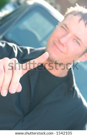 Young man wearing black shirt is pointing his index finger out as he leans back against his truck