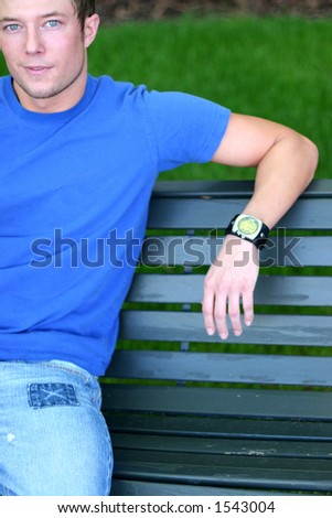 Young man in blue shirt is sitting down on bench