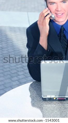 Blond hair blue eye business man is talking on his cellphone with his laptop in front of him in a business building plaza