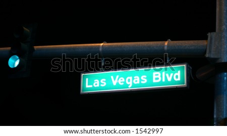 Lit up green Las Vegas Blvd. street sign with green light against dark night
