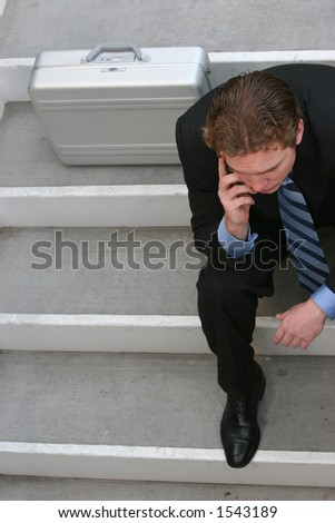 Business man in dark blue suit is sitting down talking on his cellphone next to his briefcase