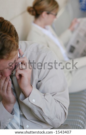 Business team dressed in tan clothes take a break; business woman is reading a paper, and man is talking on the cellphone