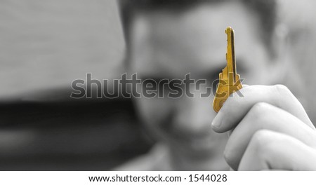 Young man smiles in the background as he holds in his hand the very golden key to success