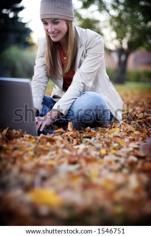 Woman dressed in fall clothing types on her laptop as she sits in the fallen leaves