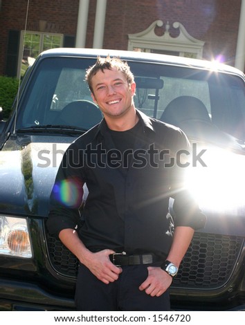 Younger man dressed in black is standing next to his black truck