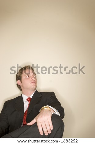 Business man in black suit is holding one leg as he sits crossed legged