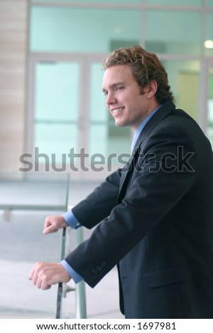Business man in dark suit, blue shirt, and blue tie stands over glass with smile