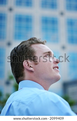 Businessman Stands with confidence and Looks Away with a blue button down shirt in front of a business building