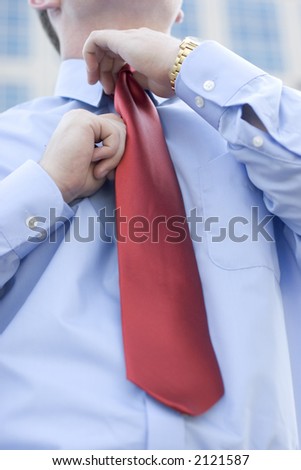 Businessman adjusting his red tie while he wears his gold watch and blue button down shirt