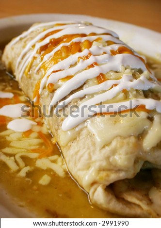 Stuffed burrito lies on a plate in the restaurant covered with sour cream and green sauce ready to be eaten