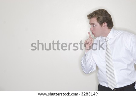 Businessman standing in his office puts his finger to his lips to have silence