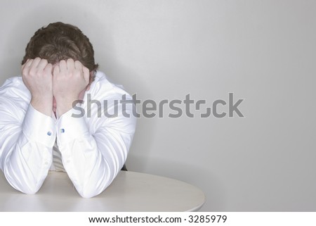 businessman sitting at his desk hides his face in frustration