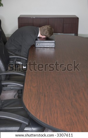 Businessman sleeps on his briefcase in the conference room at the end of the table
