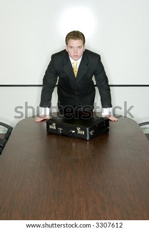 Businessman stands at the head of the conference table with his briefcase in front of him