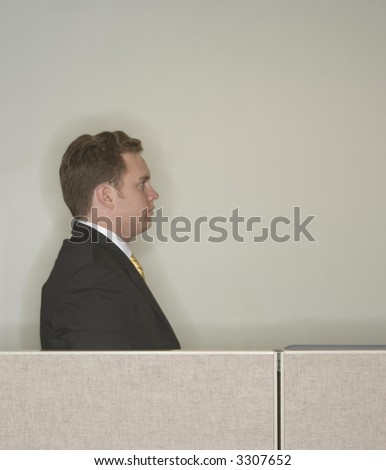 Businessman looks ahead and stares away from the camera as he gives his profile standing behind the office cubicle wall