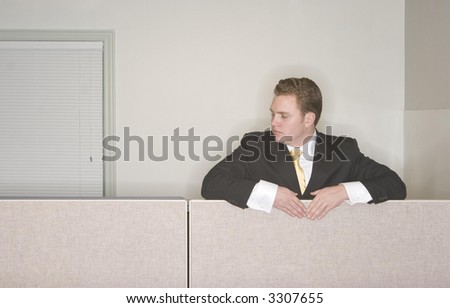 Businessman looks down from  his cubicle in his office while wearing a black suit and gold tie