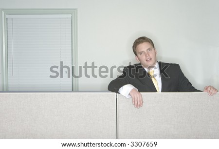 Businessman is bored and sits above his cubicle in his office looking at the camera with his business suit on