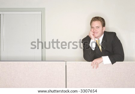 Businessman smiles with his hand on his chin standing above his office cubicle