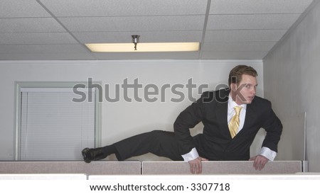 Businessman attempts to climb up over his cubicle in an attempt to get out of his office while looking at the camera