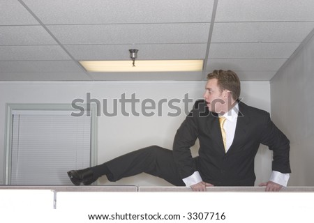 Businessman attempts to climb over his cubicle trying to escape out of his office while wearing a black suit