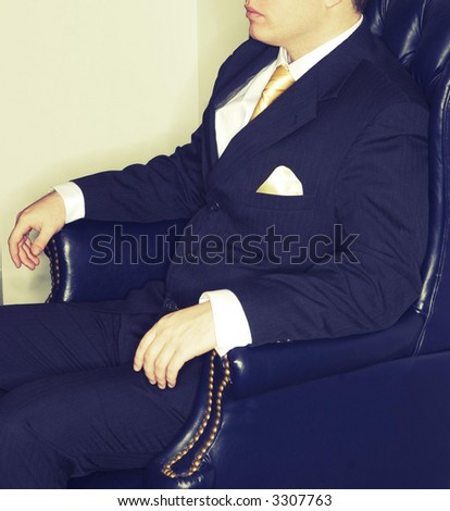 Businessman sitting in a comfy business chair with his arms out wearing a black suit and gold tie