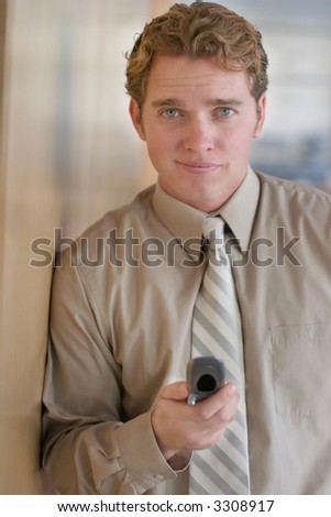 Businessman stands against the wall holding his cell phone in his hand with a smile on his face