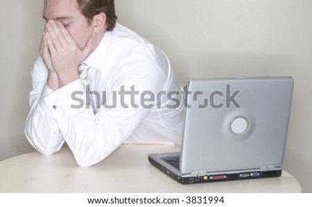 Businessman sits at his table with his head in his hands while wearing a white business shirt next to his laptop