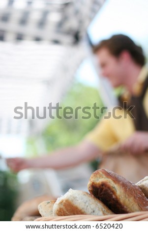 One young man making purchase at farmers market with focus on basket of bread in foreground