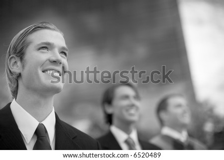 black and white three business people in a row smiling in front of business building structure