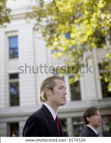 head and shoulders shot of two businessmen in full suits profile sideways view against building structure and tree