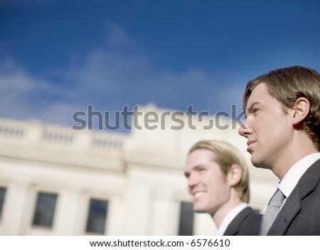 head and shoulders view of two business men well dressed standing side by side next to courthouse looking away