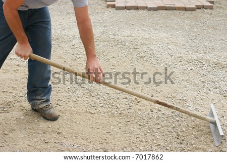 close up of one male construction worker bending over pushing rake leveling dirt