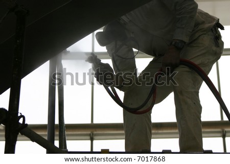 close-up view of one man bending over holding sprayer painting part of building