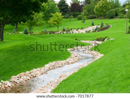 stream of water flowing through grassy hills with trees