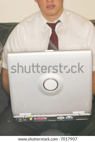 front close-up view of young man with loose tie holding laptop on knees as he sits on sofa