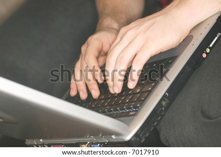 unique close-up angle of young man typing on laptop which is resting on his knees as he sits on sofa