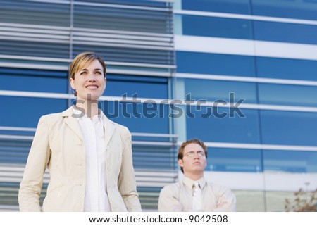 businesswoman and businessman standing side by side with arms folded looking forward
