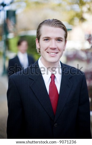 two businessmen staggered one behind the other in full suits with first man smiling