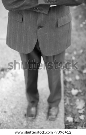 waist-down front shot of businessman folding arms wearing suit standing on sidewalk