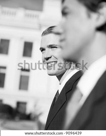 two businessmen standing side by side smiling looking forward