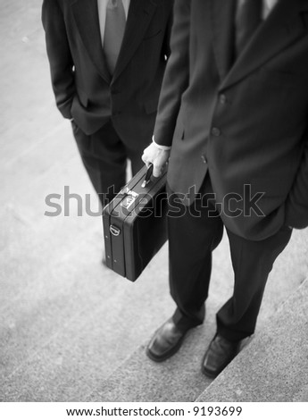 two businessmen standing on steps with hands in pockets and holding briefcase no faces