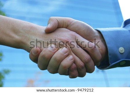 close up handshake with blue office building in background