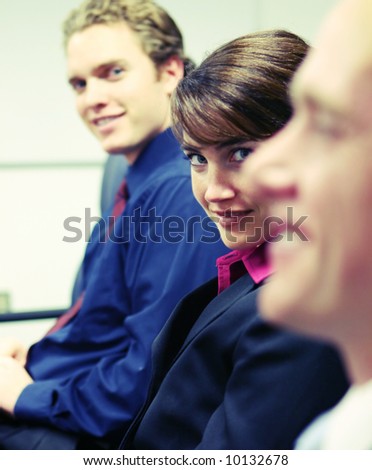 woman sitting between two men looking at camera in boardroom meeting