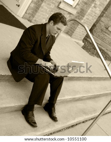 Business man is sitting on steps and typing on laptop wearing full suit with focused expression
