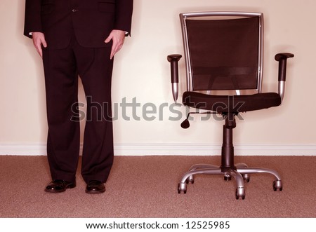 Businessman wearing full suit with hands on his sides standing next to empty chair. Concept: Office Life
