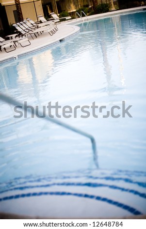 Hand rail going down into swimming pool with chairs and a fence in the background
