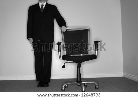 Businessman in full suit and tie stands next to empty office chair