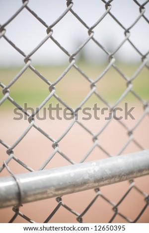 close-up of a baseball fence outside in the summer with a chain link fence in the front and a baseball field in the background