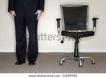 Businessman wearing full suit stands next to empty office chair